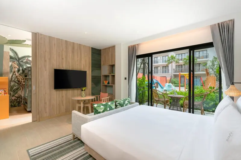 Chambre lumineuse avec un lit blanc et un coin salon donnant sur une terrasse.
