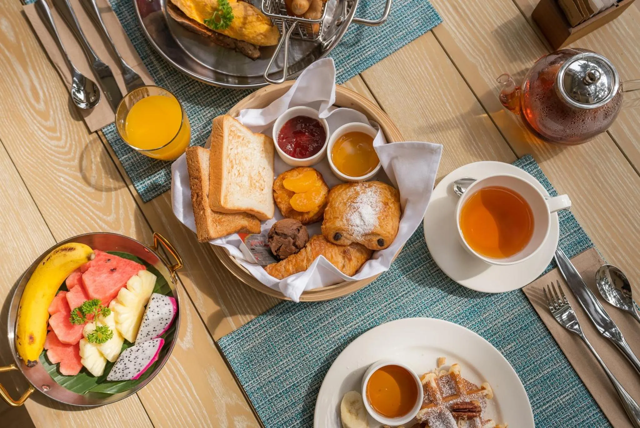 Une table est dressée avec un petit-déjeuner copieux composé de viennoiseries, de fruits frais et de boissons.