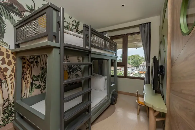 Lit superposé dans une chambre décorée de motifs animaliers avec vue sur la végétation.