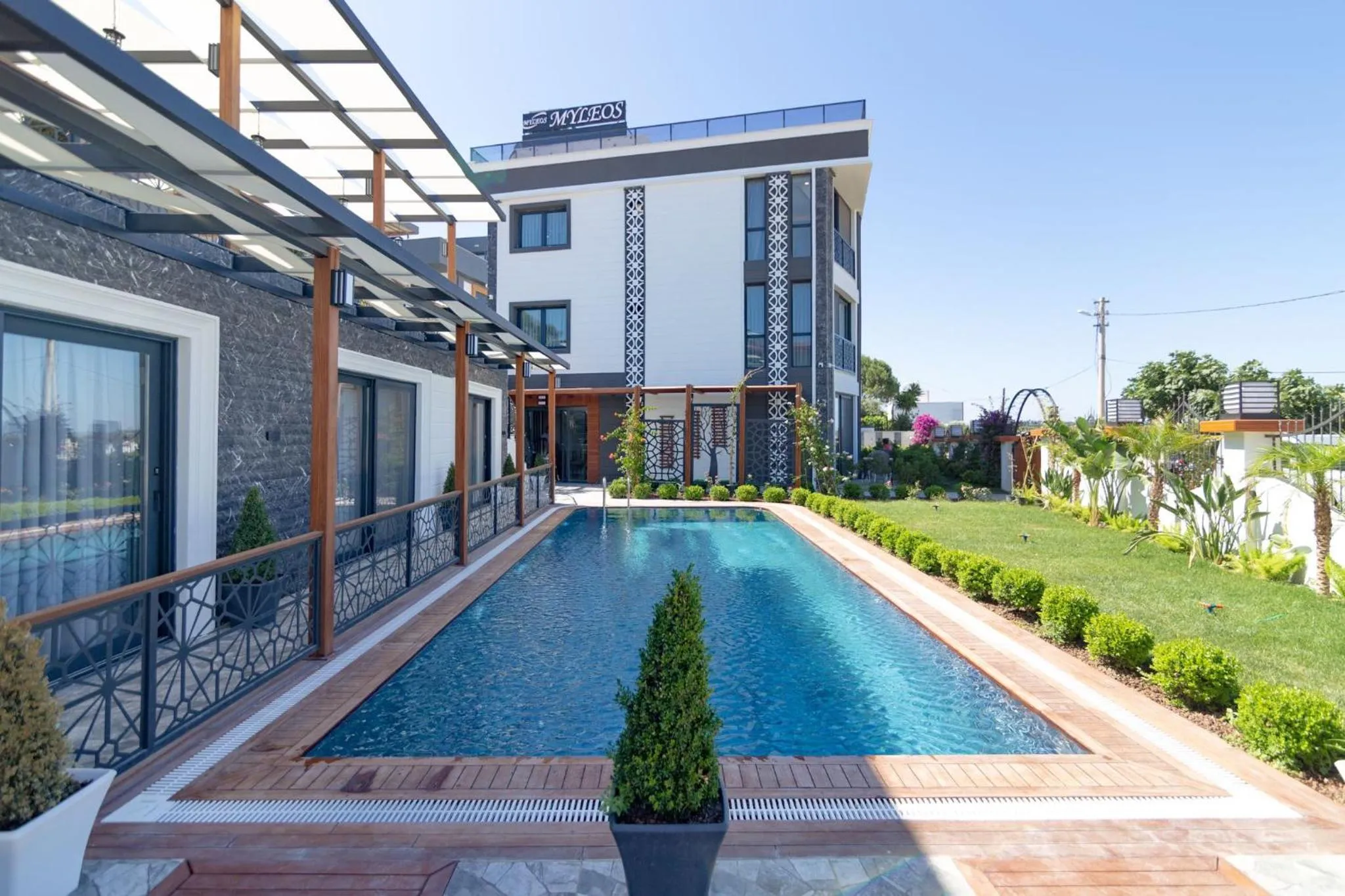 Une piscine rectangulaire bordée d'une terrasse ensoleillée devant un bâtiment moderne.