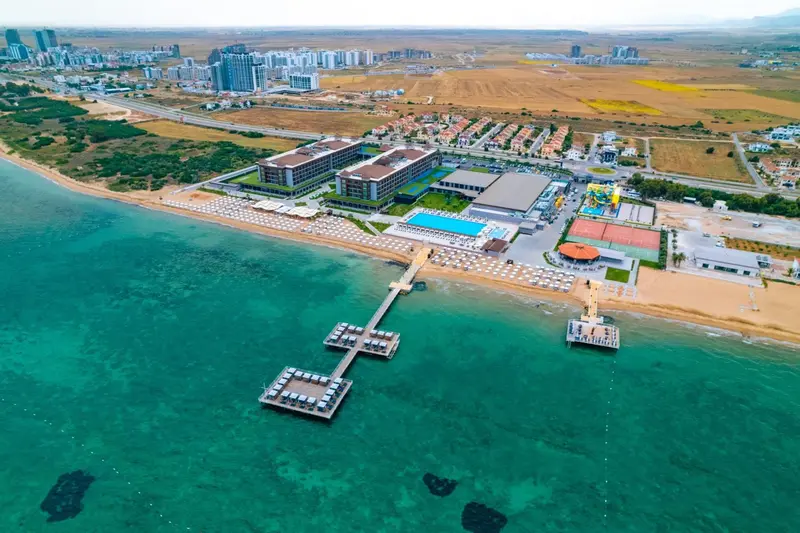 Vue aérienne d'un complexe hôtelier avec piscine et pontons sur une plage turquoise.