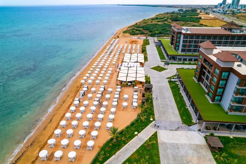Vue aérienne d'une plage de sable avec des transats et des parasols devant un bâtiment moderne.