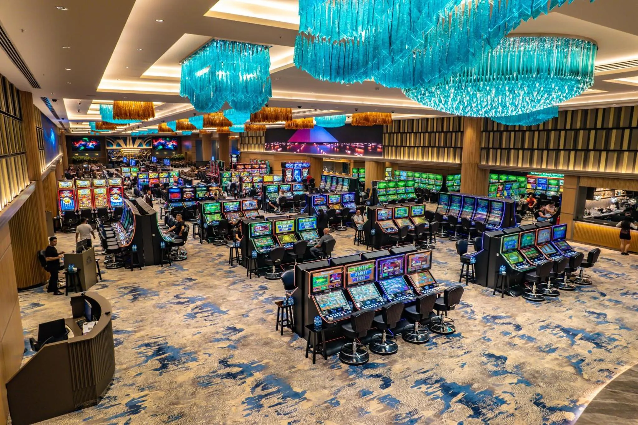 Vue d'ensemble d'une salle de jeux avec de nombreux machines à sous et quelques personnes assises.