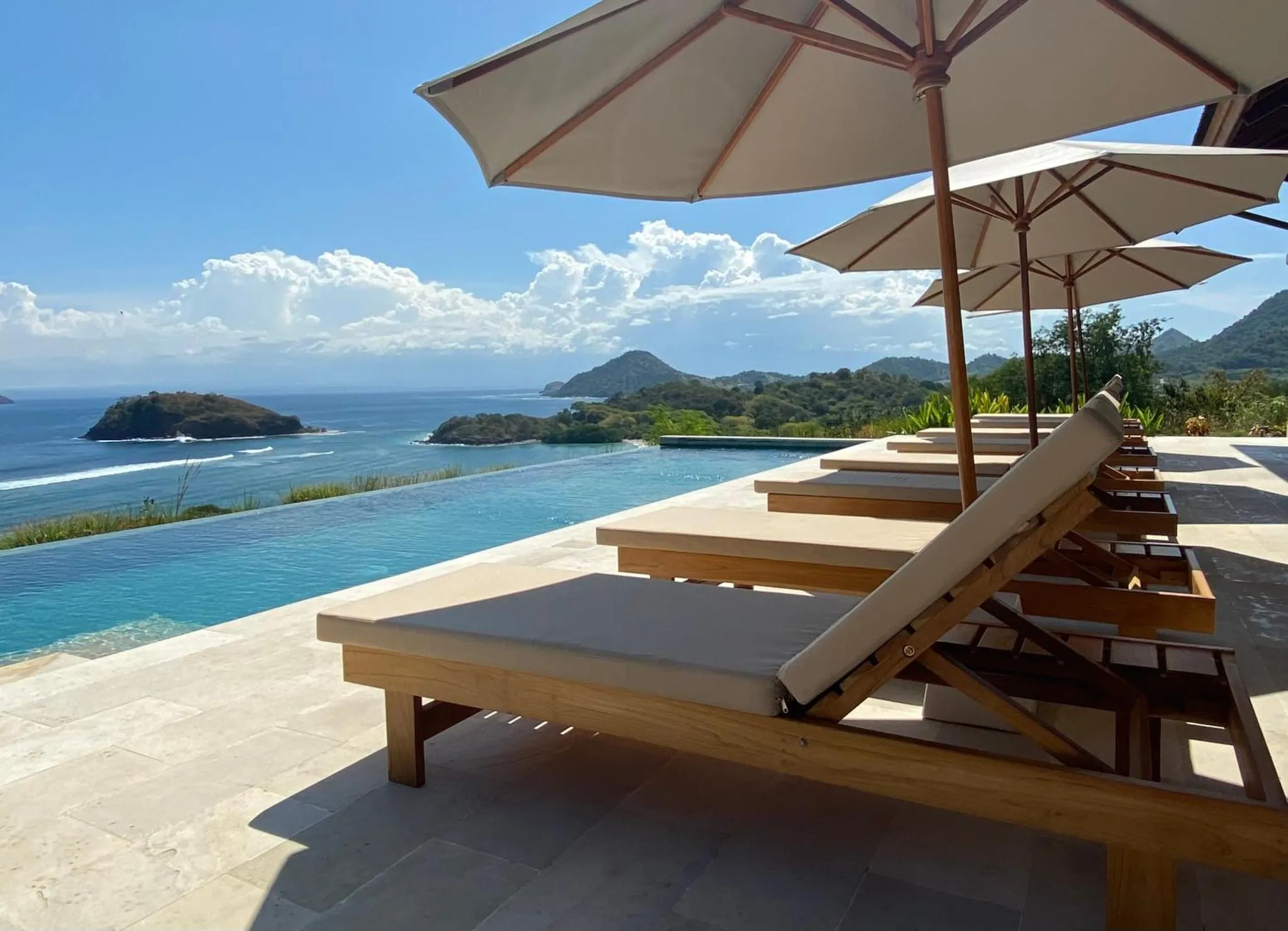 Transats en bois au bord d'une piscine à débordement avec vue sur la mer et les îles.