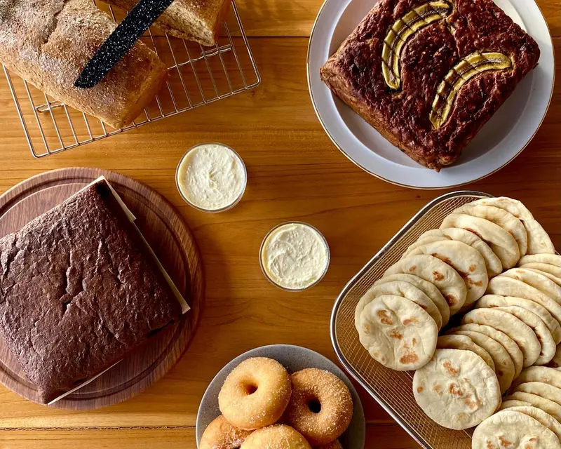 Assortiment de pains, de viennoiseries et de tartinables présentés sur une table en bois.