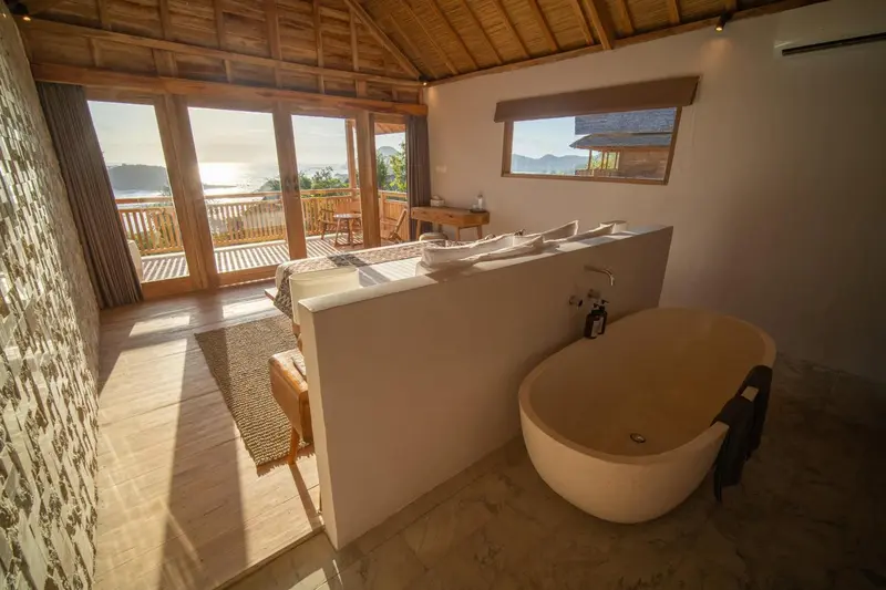 Une baignoire blanche se trouve dans une salle de bain lumineuse avec vue sur la mer.
