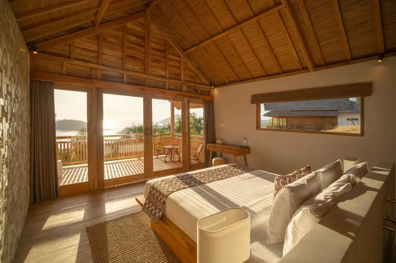 Chambre lumineuse avec un grand lit et une vue sur la mer depuis une terrasse.