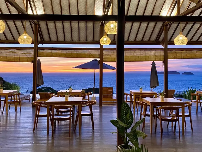 Terrasse avec tables et chaises donnant sur la mer au coucher du soleil.