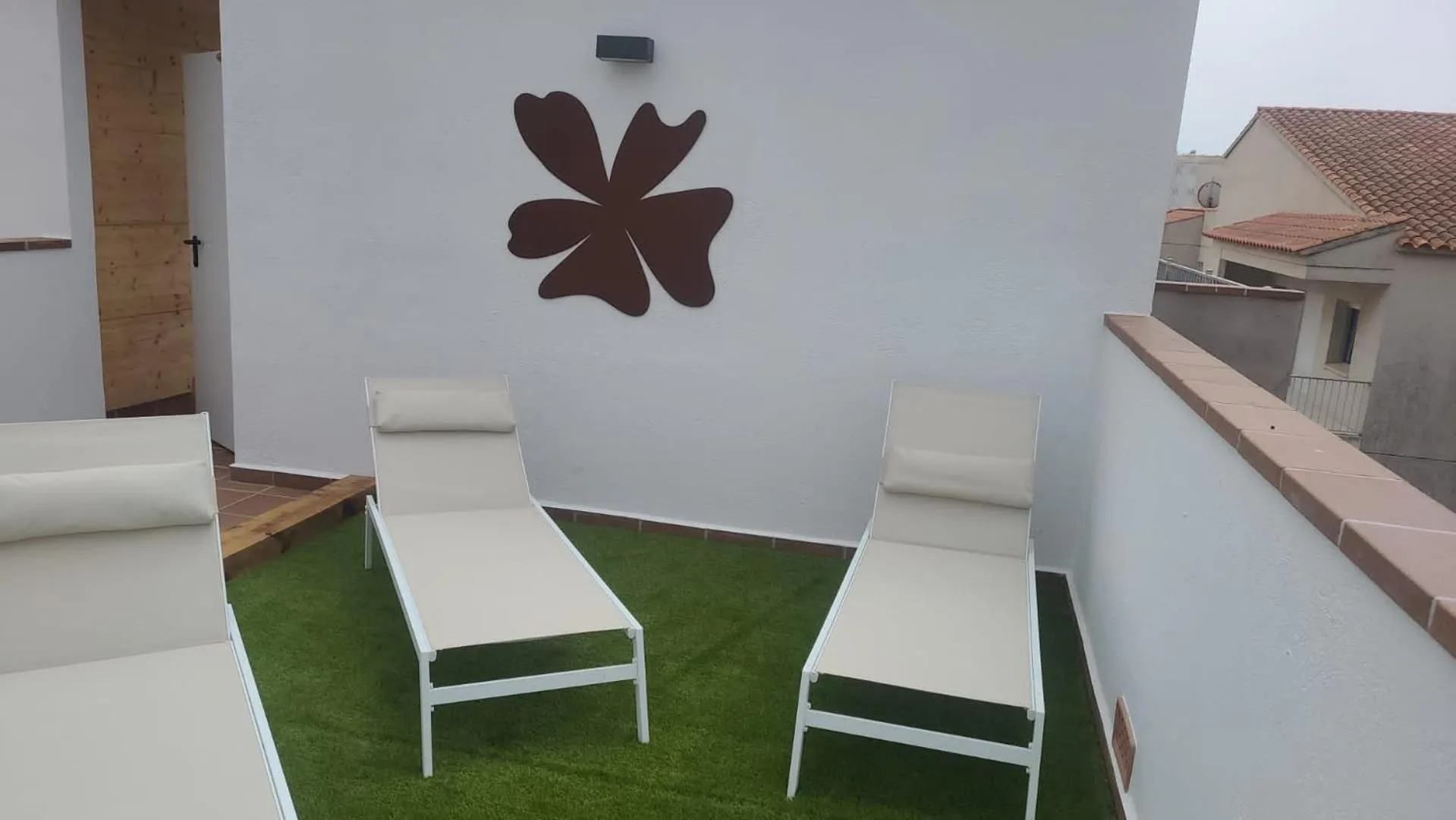 Deux transats blancs sur une terrasse avec gazon artificiel et un décor mural.