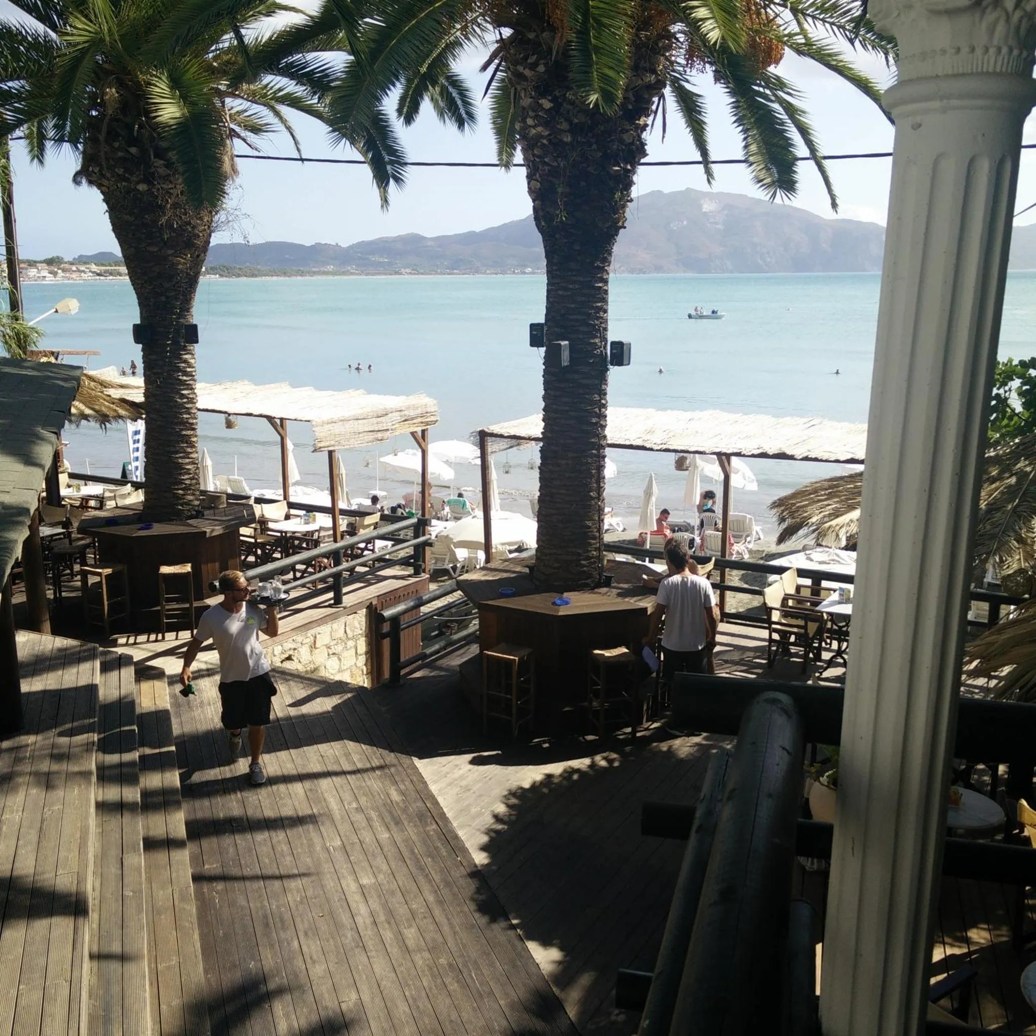 Terrasse ombragée avec tables et chaises donnant sur la mer.
