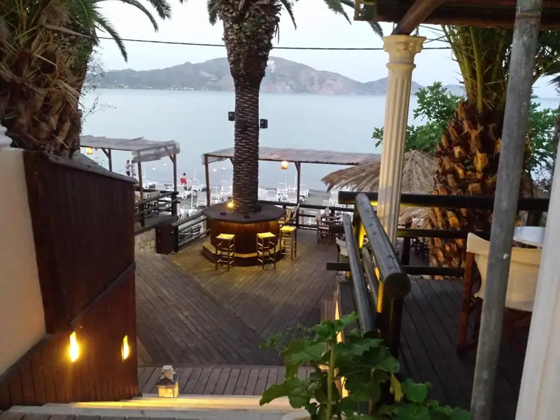 Terrasse en bois avec tables et chaises, vue sur la mer au loin.