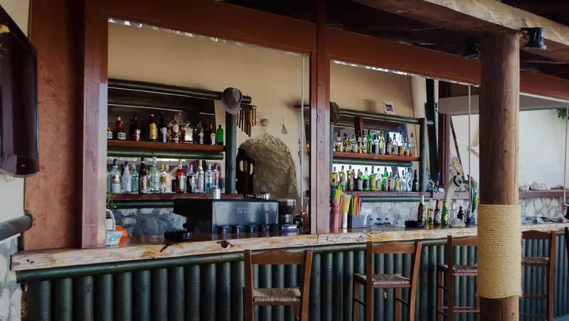 Un comptoir de bar en bois avec des bouteilles et des tabourets.