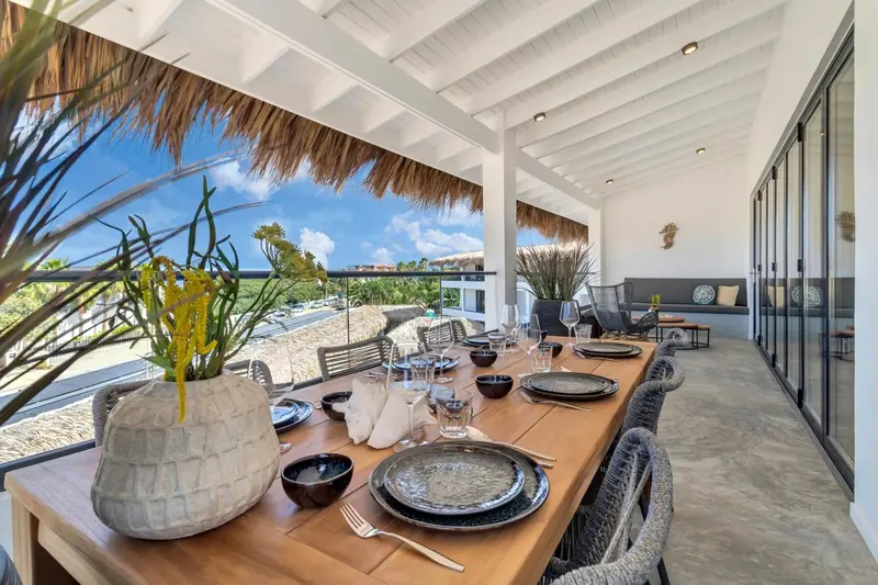 Une table est dressée pour un repas sur une terrasse ombragée.