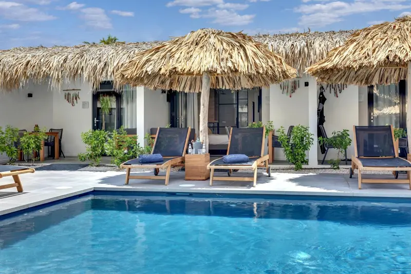 Transats et parasols en chaume bordent une piscine turquoise.