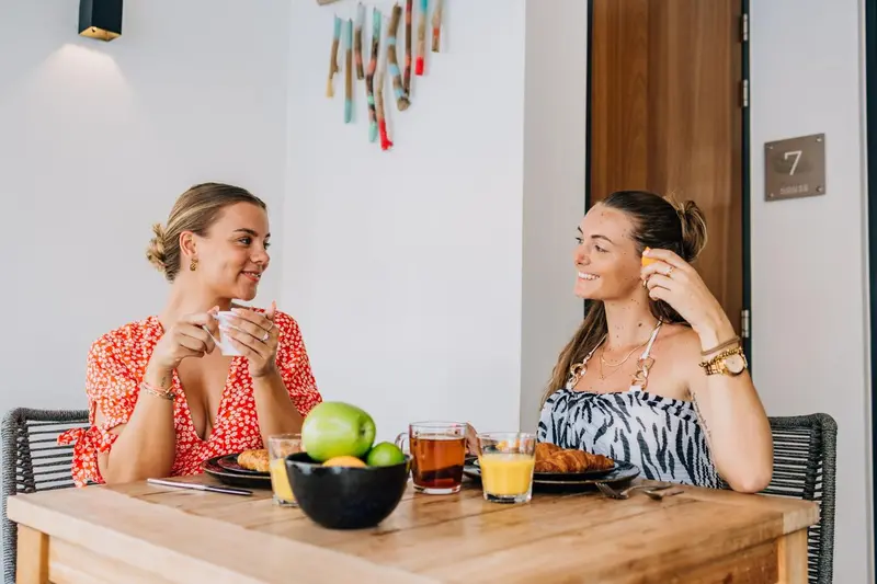 Deux femmes sourient en prenant leur petit-déjeuner à une table en bois.