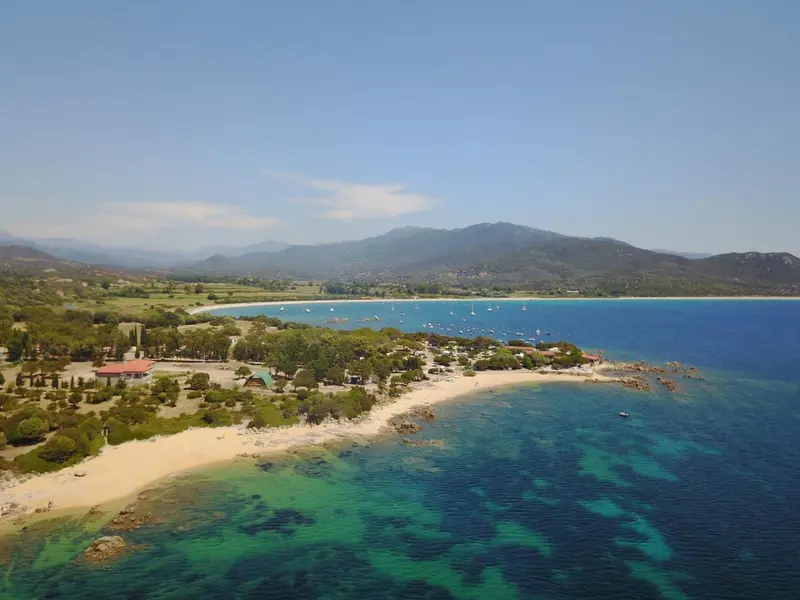 Vue aérienne d'une plage de sable fin bordée d'une eau turquoise et de végétation luxuriante.