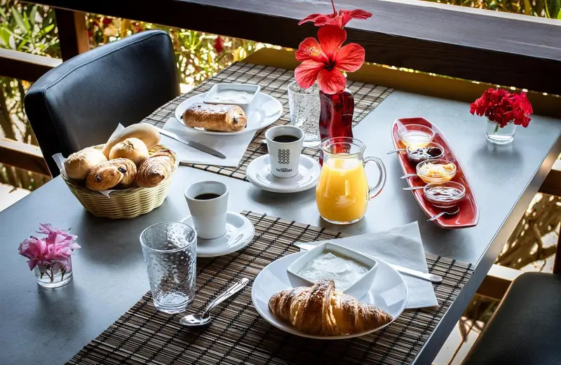 Une table est dressée pour le petit-déjeuner avec des viennoiseries, des fruits et des boissons.