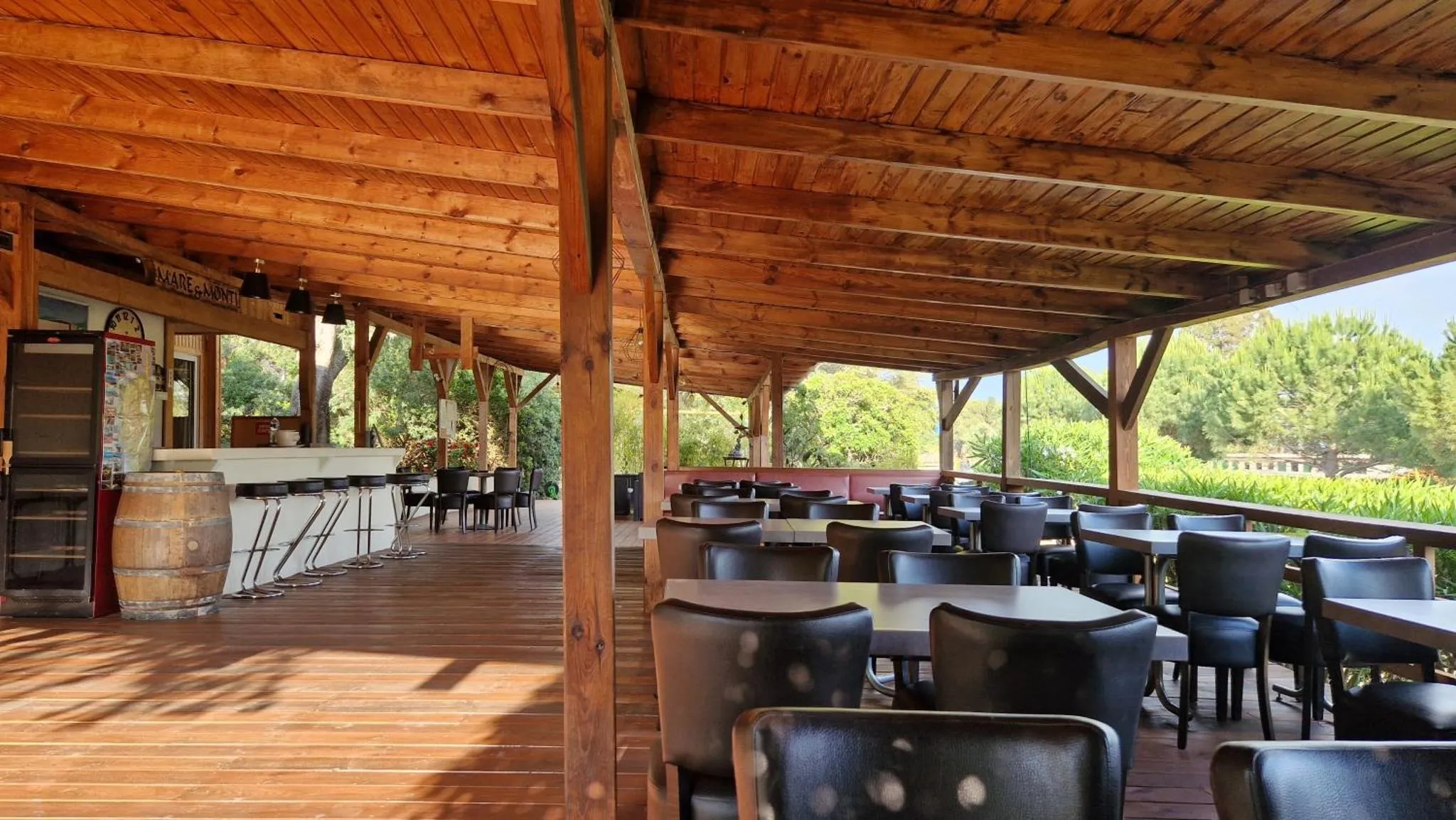 Terrasse ombragée avec tables et comptoir de bar.