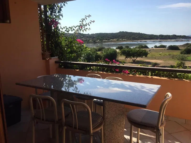 Une table et des chaises composent un espace repas sur une terrasse ensoleillée avec vue sur un paysage marin.