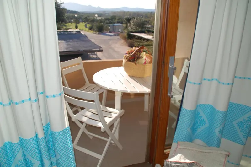 Une table ronde et des chaises blanches sur un balcon avec vue sur un paysage montagneux.