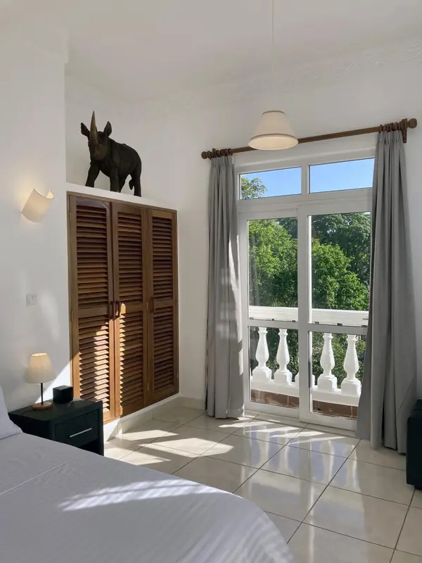 Une chambre lumineuse avec un lit blanc et une vue sur une végétation luxuriante.