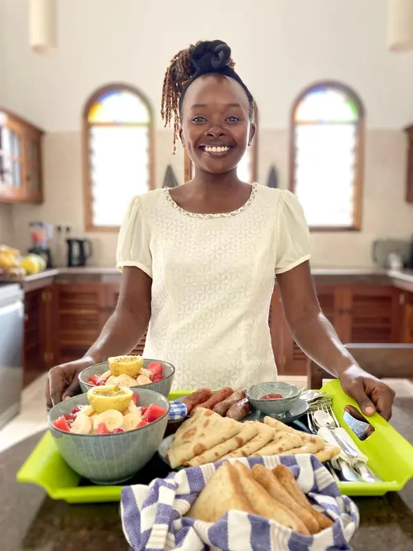 Une personne souriante présente un plateau de fruits et de viennoiseries.
