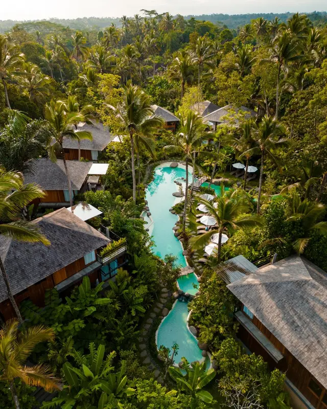 Vue aérienne d'un complexe hôtelier avec piscine sinueuse au milieu d'une végétation luxuriante.