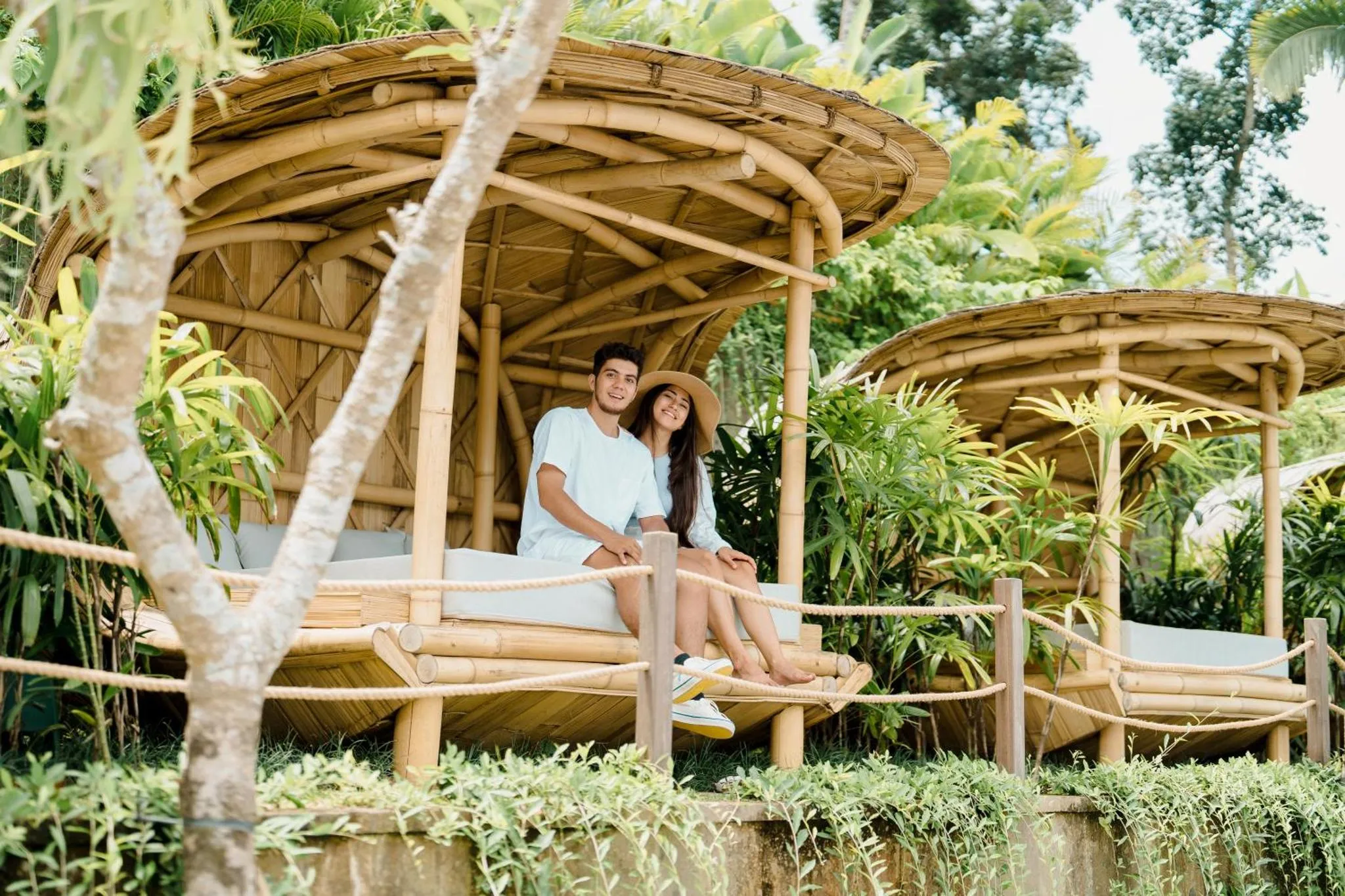 Un couple souriant se détend sur une terrasse en bambou ombragée.