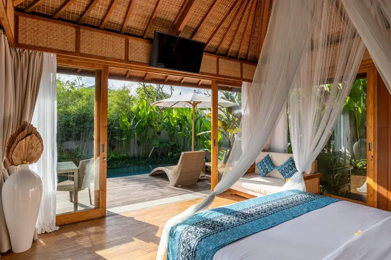 Une chambre lumineuse s'ouvre sur une terrasse avec piscine et végétation tropicale.