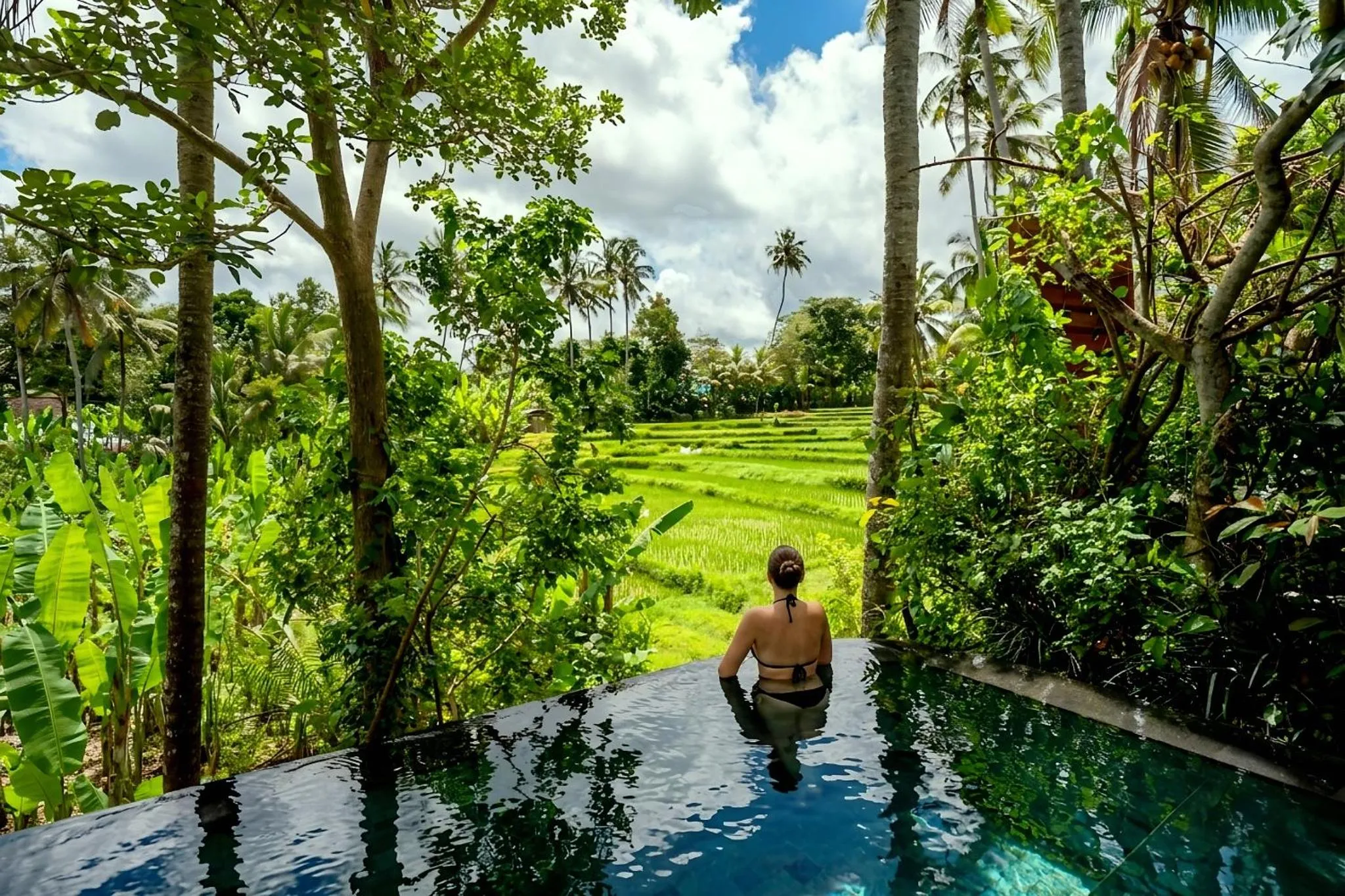 Une personne se détend dans une piscine à débordement au milieu d'une végétation luxuriante.