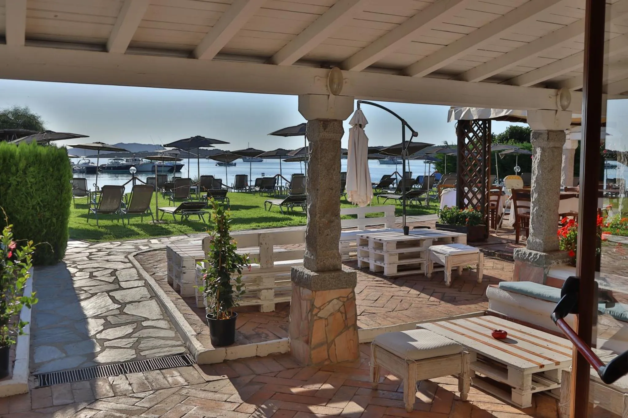 Terrasse ombragée avec mobilier en bois et vue sur la mer.