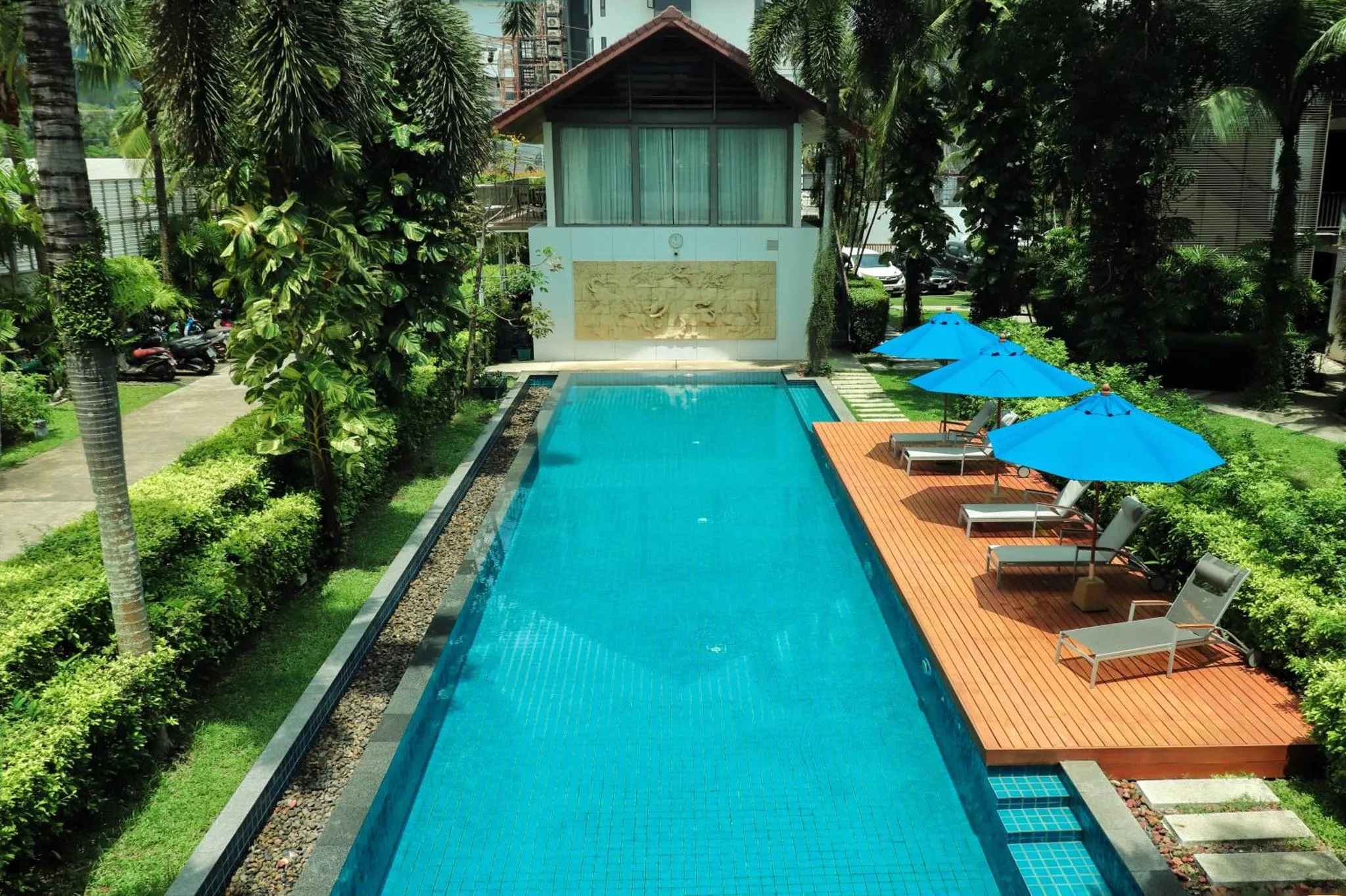 Une piscine rectangulaire bordée d'une terrasse en bois avec des transats bleus sous des parasols.