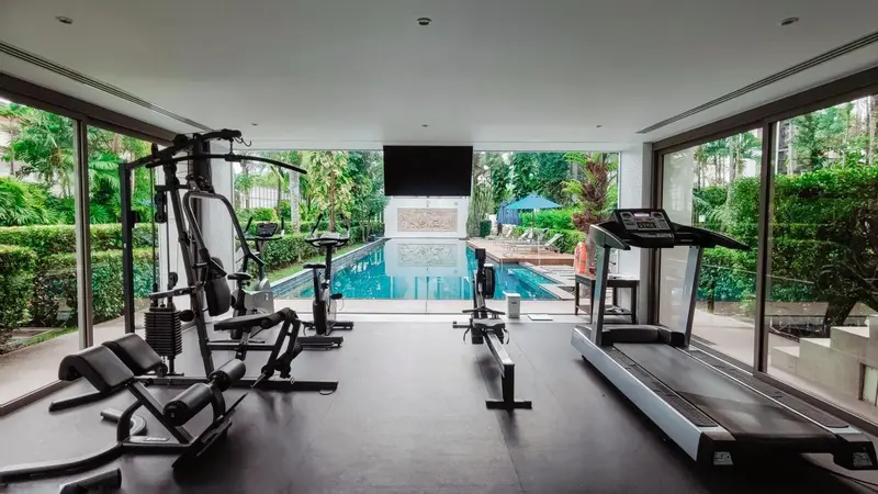 Une salle de sport lumineuse donne sur une piscine et une végétation luxuriante.