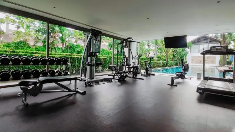 Une salle de sport lumineuse avec des équipements de musculation et une vue sur une piscine et une végétation luxuriante.