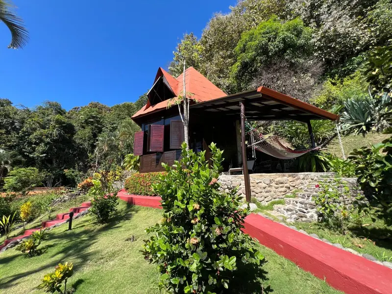 Une maison de bois sur pilotis avec une terrasse ombragée et un jardin tropical.