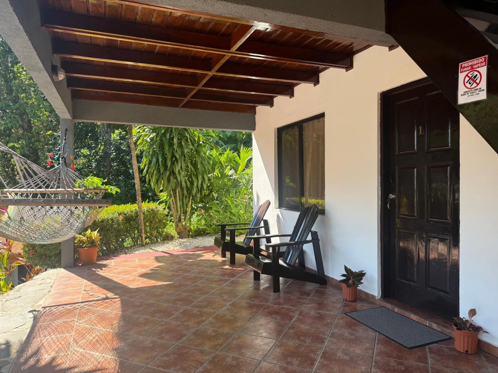 Terrasse ombragée avec hamac et mobilier de jardin devant une entrée.