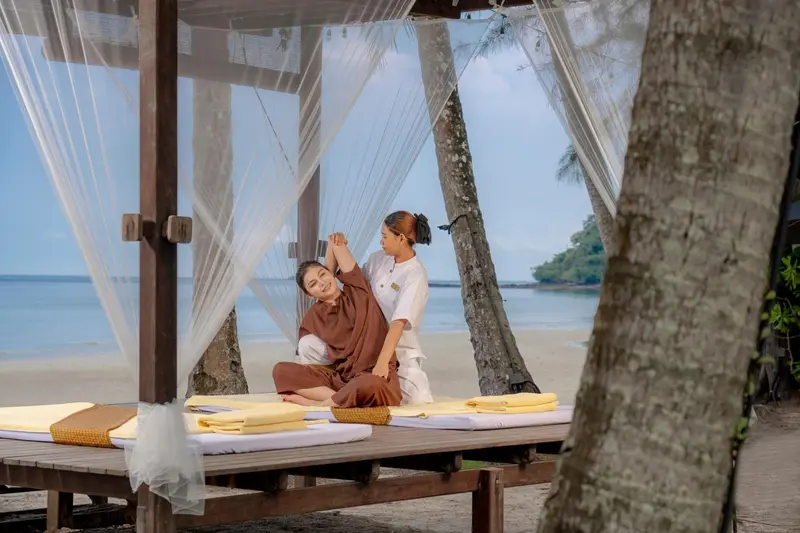 Une femme reçoit un massage sur une plateforme en bois face à la mer.