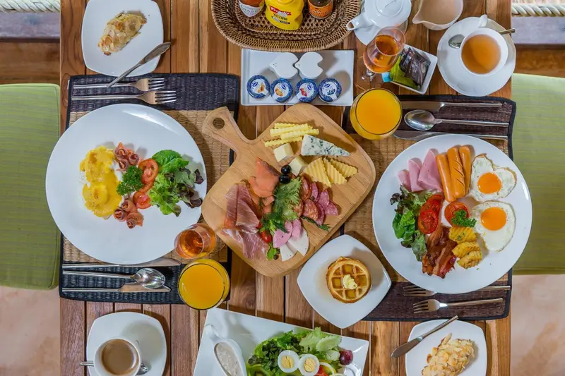 Table dressée pour un copieux petit-déjeuner avec œufs, charcuterie et viennoiseries.