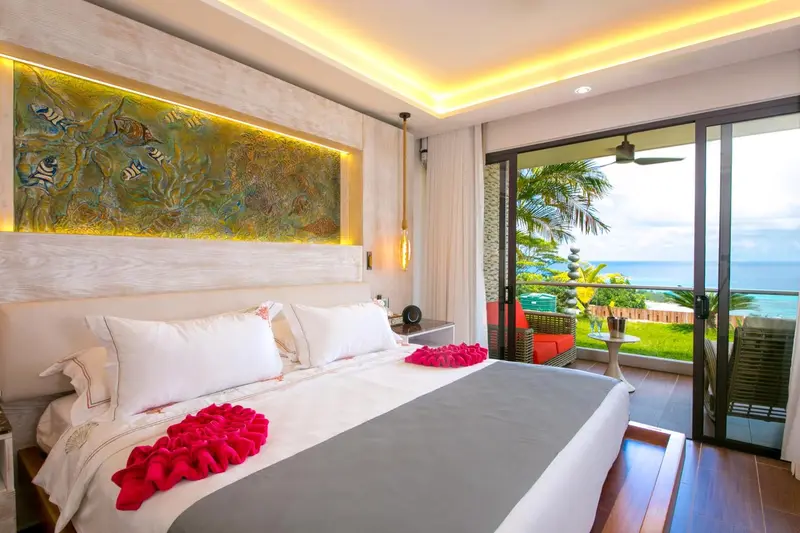 Une chambre avec un grand lit décoré de fleurs, donnant sur une terrasse et une vue sur la mer.