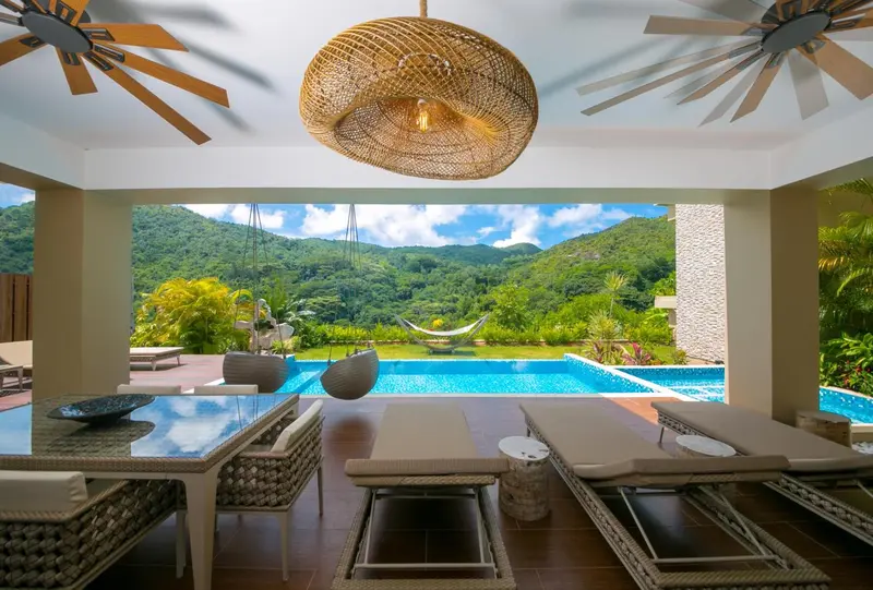 Terrasse ombragée donnant sur une piscine et un paysage montagneux.
