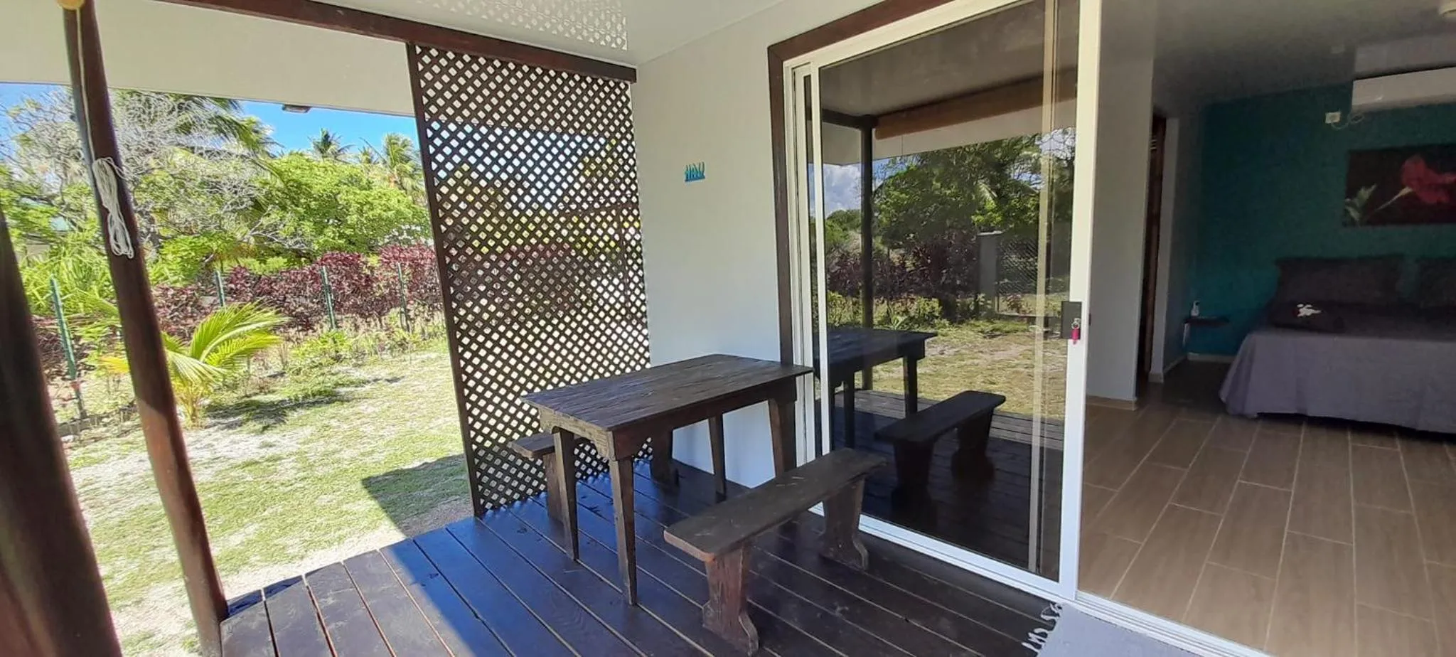 Terrasse en bois avec table et bancs donnant sur un jardin tropical.