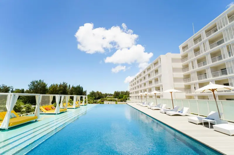 Une piscine rectangulaire bordée de transats blancs et de parasols.