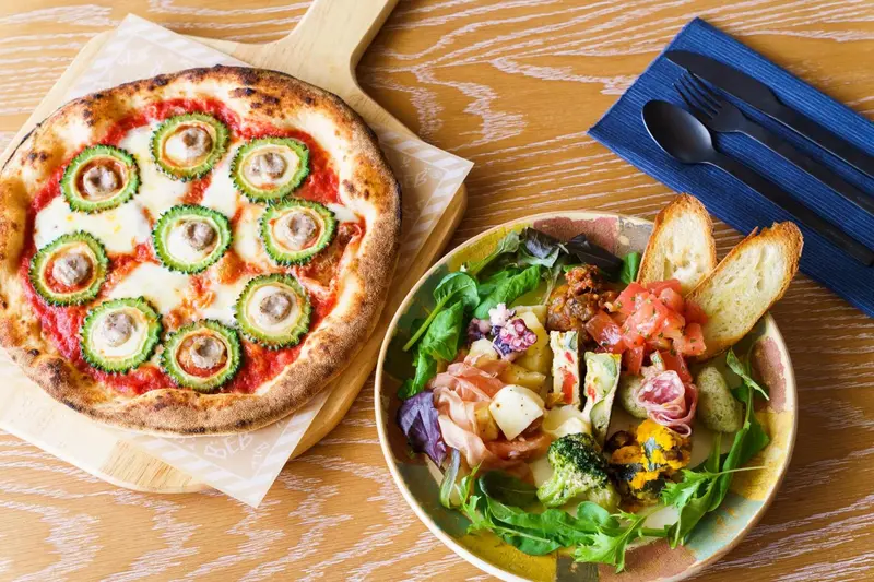 Une pizza et une salade colorée sont présentées sur une table en bois.