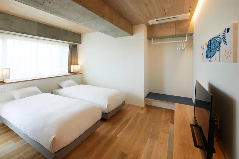 Chambre lumineuse avec deux lits simples et une décoration murale.