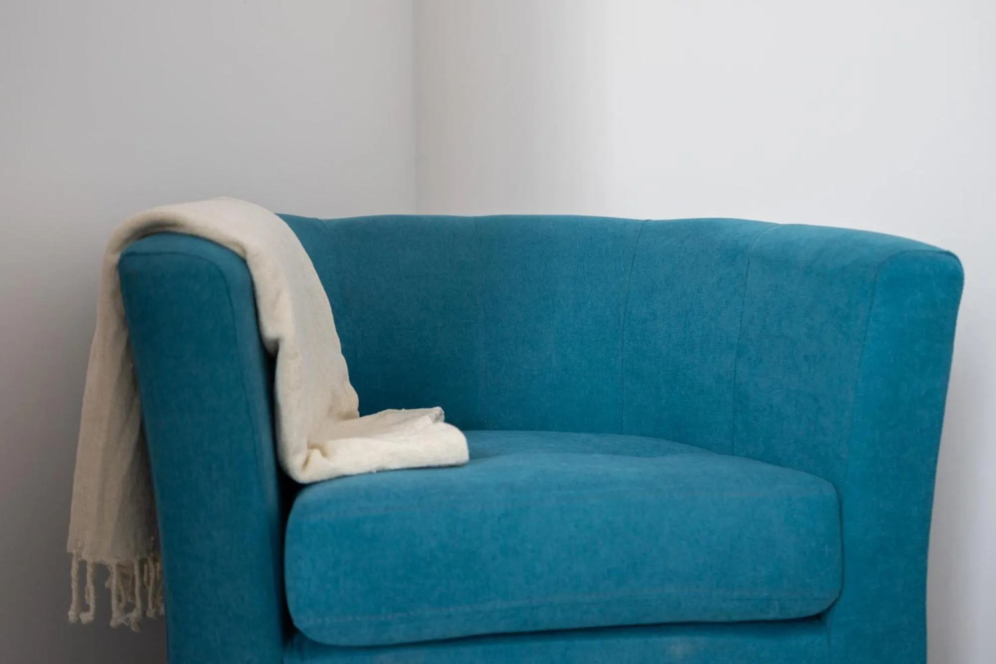 Un fauteuil bleu turquoise avec un plaid blanc.