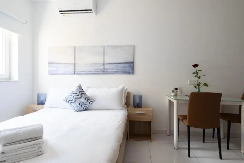 Une chambre lumineuse avec un lit fait et un coin repas.