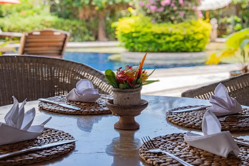 Une table dressée avec couverts et fleurs près d'une piscine.