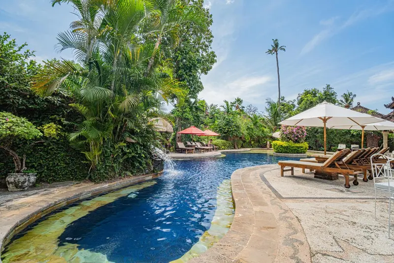 Une piscine sinueuse bordée de chaises longues et de végétation tropicale.