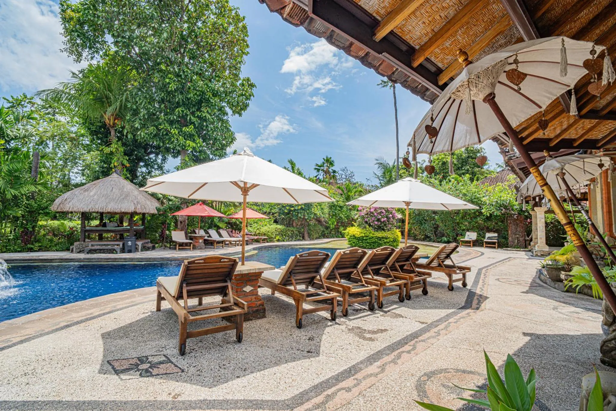 Transats et parasols ombragent une terrasse en pierre près d'une piscine.