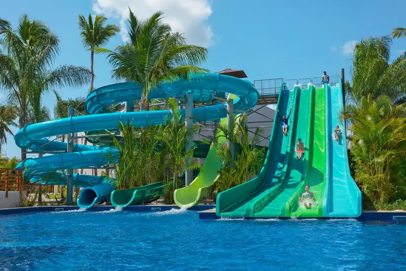 Des toboggans aquatiques colorés se jettent dans une piscine turquoise entourée de végétation tropicale.